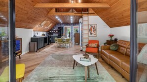 A spacious loft with a wooden ceiling, a dining area, a kitchen, and a living room with a leather sofa.