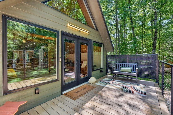 A modern house with large glass doors, a deck, and a bench.