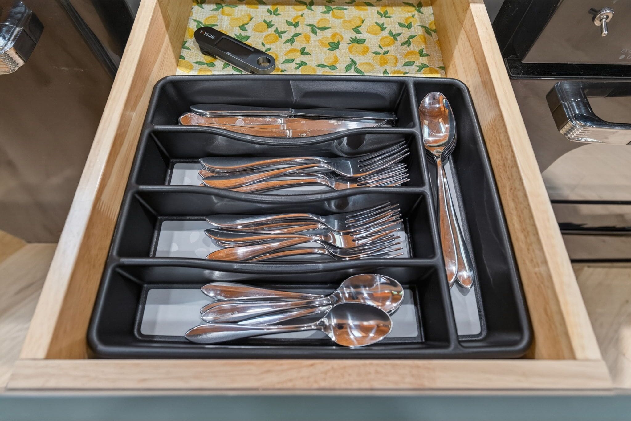 A drawer with a black interior containing multiple forks, spoons, and a knife.