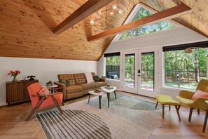 Ein geräumiges Wohnzimmer mit hoher Holzbalkendecke, einem großen Fenster und einer gemütlichen Sitzecke.