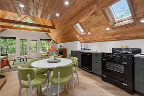 A modern kitchen with a wooden ceiling, a round dining table with chairs, and a large oven.