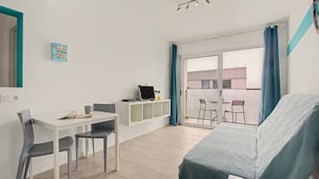 Una habitación con cama, escritorio, dos sillas, computadora y vista a un área exterior con mesa y sillas.