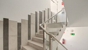 A staircase with a metal handrail and a fire extinguisher mounted on the wall. - B-Rent Bristol Beach Surf & Fun – Your Perfect Fuerteventura Getaway (Corralejo)
