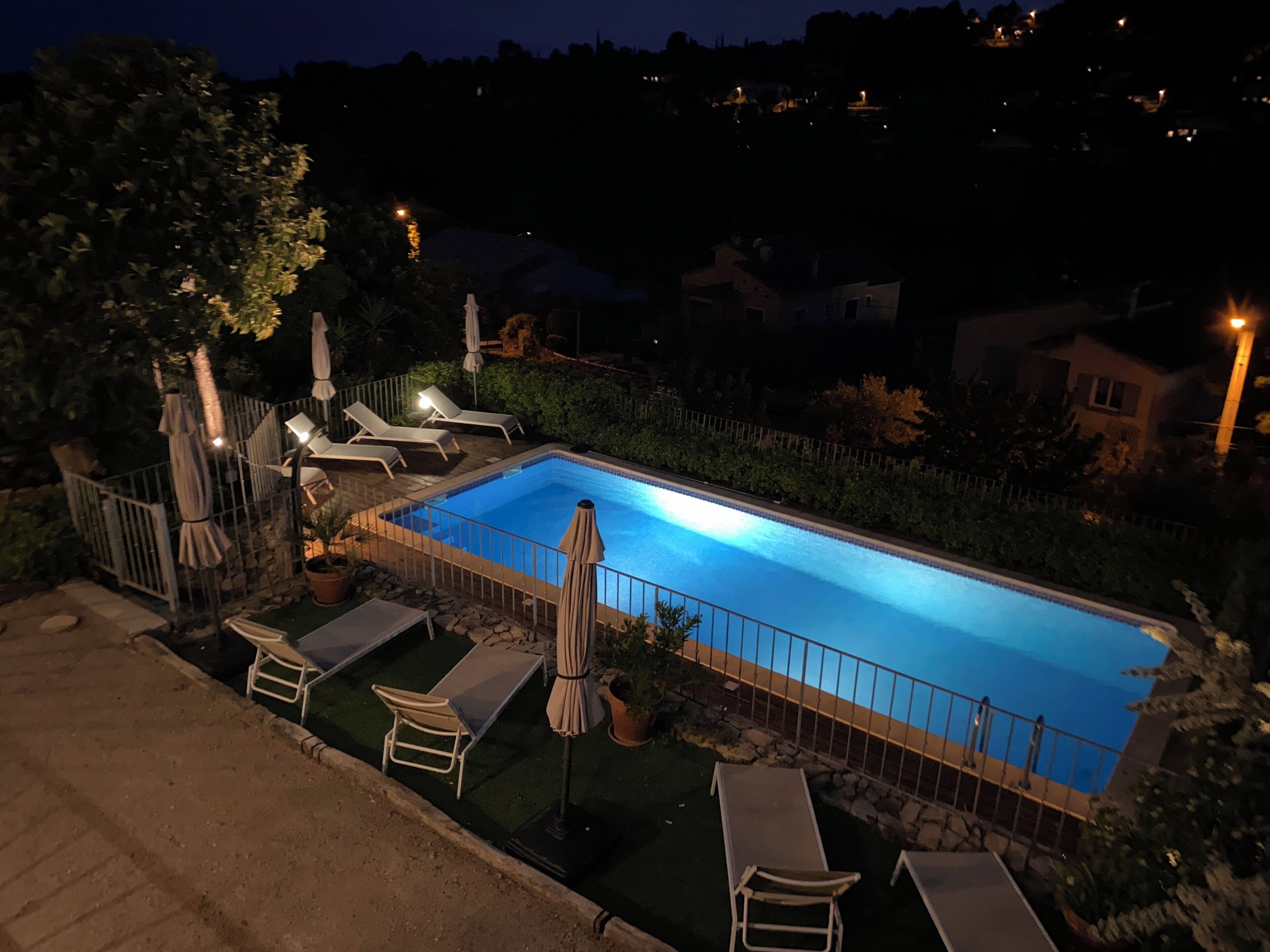 A swimming pool with lounge chairs and umbrellas, surrounded by a stone wall and greenery.