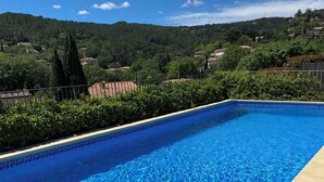 Ein rechteckiger Pool mit blauen Fliesen, umgeben von einer Holzterrasse und einem Metallzaun.