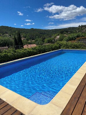 A rectangular swimming pool with blue tiles, surrounded by a wooden deck and a metal fence. - Cozy family villa in Provence with a large terrace, pool, and village life right nearby. (Cotignac)