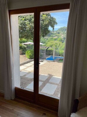 A room with a sliding glass door leading to an outdoor area with a pool and garden. - Cozy family villa in Provence with a large terrace, pool, and village life right nearby. (Cotignac)