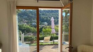 Ein Schlafzimmer mit Bett, einem Sessel und einer Glasglastür, die auf einen Balkon mit Blick auf eine Hügel- und Gartenlandschaft führt.