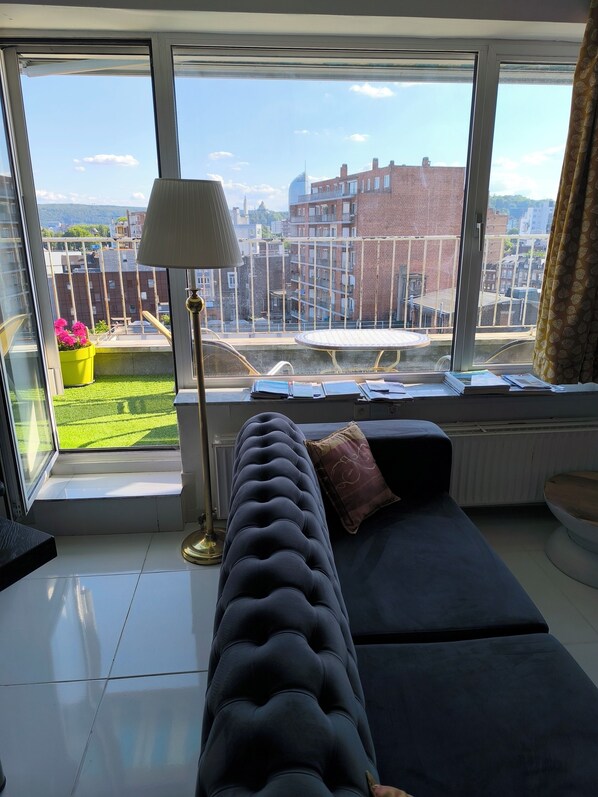 A modern living room with a large window, a sofa, a lamp, and a view of the cityscape. - Center Liège Médiacité, rue Libotte 34, panoramic terrace, flat for 2 (Liège)