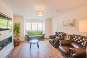 A living room with a sofa, two armchairs, a small round table, a TV, a plant, and a painting on the wall. - Dunmore East Sunrise Meadows (Dunmore East)