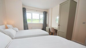 Een slaapkamer met twee bedden, een bureau en een raam met gordijnen.