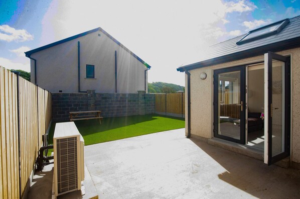 A house with a patio, a small lawn, and a sliding glass door leading to an outdoor area. - Dunmore East Sunrise Meadows (Dunmore East)