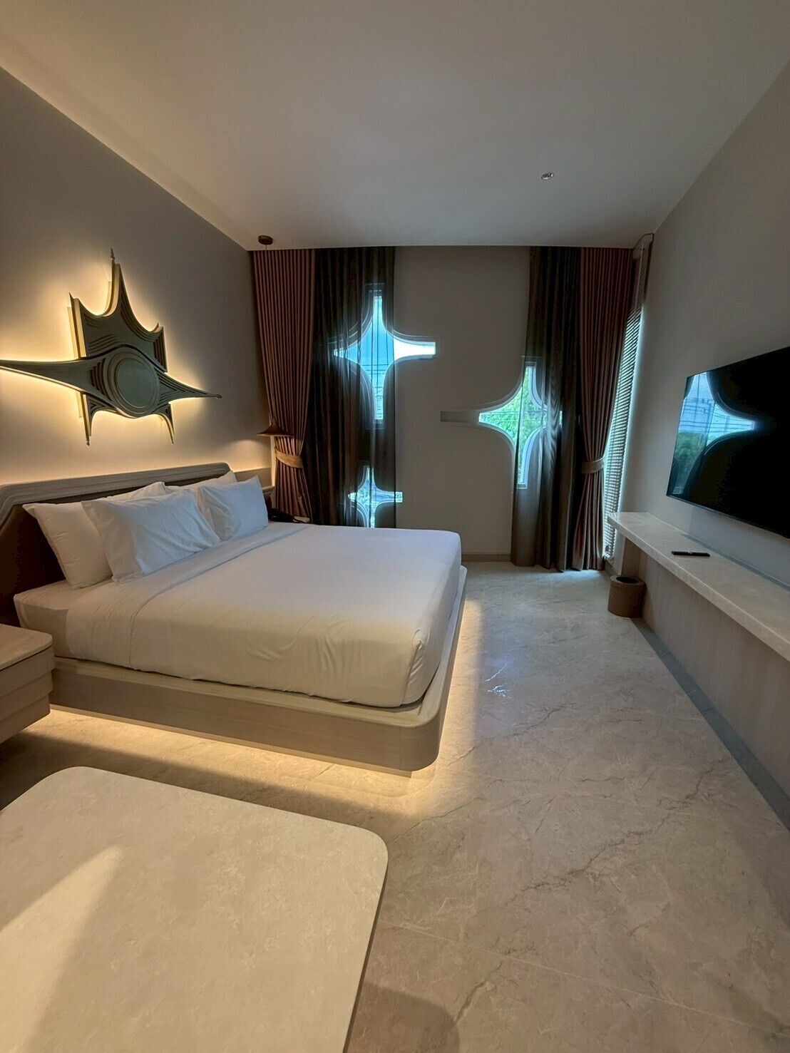 A modern hotel room with a large bed, a flat-screen TV, and a unique star-shaped light fixture.