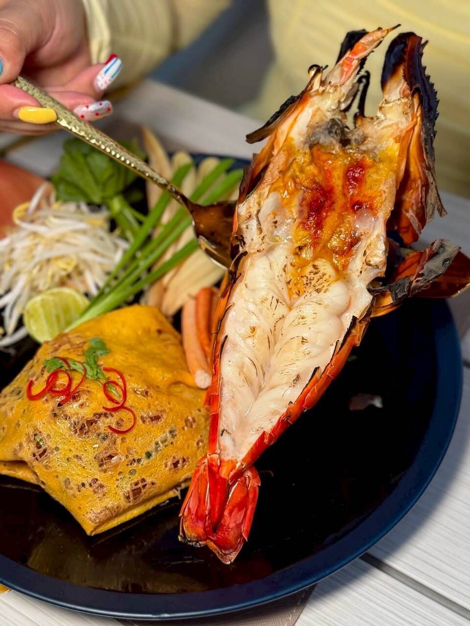 A lobster tail on a plate with a side of vegetables and a yellow condiment.