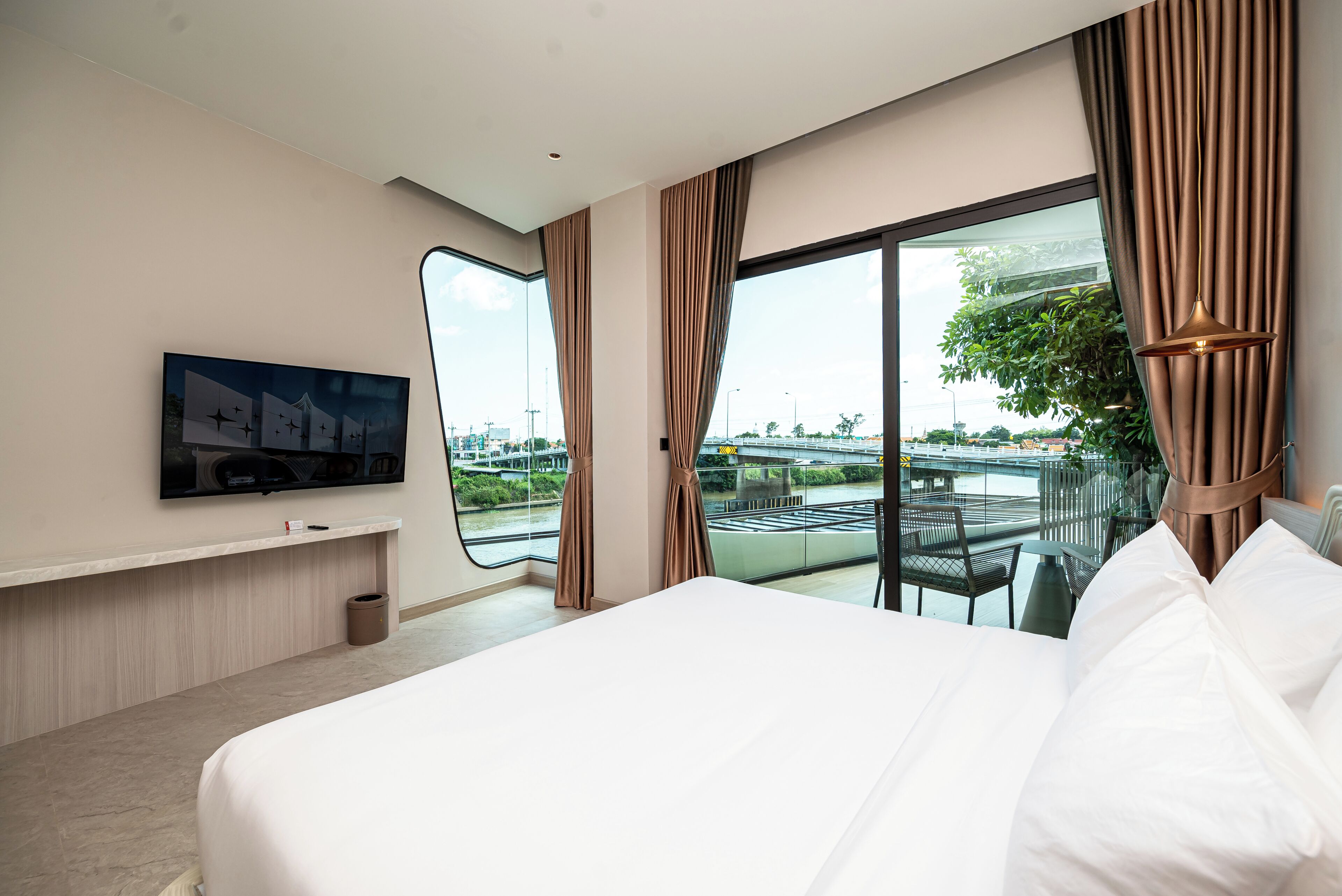 A hotel room with a large bed, a flat-screen TV mounted on the wall, and a view of a bridge and river.