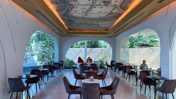 A modern dining area with round tables and chairs, large windows, and a unique ceiling design.