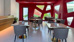 A modern dining area with tables and chairs, a reception desk, and large windows with a view. - The Rachata Ayothaya (Ayutthaya)