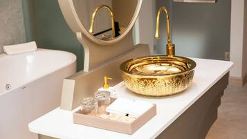 Un baño con lavamanos dorado, un espejo y encimera blanca.