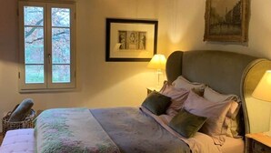 A bedroom with a bed, a window, a framed picture, and a lamp.