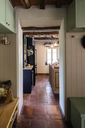 A narrow hallway with a kitchen area on the right, featuring a tiled floor and wooden beams on the ceiling.