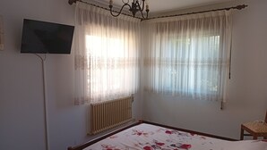 A bedroom with a bed, a radiator, a television on the wall, and two windows with sheer curtains. - Dorm 2 between Trega and Minho A GUARDA (A Guarda)