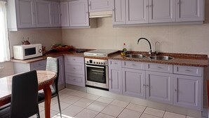 A kitchen with white cabinets, a microwave, a stove, a sink, and a chair. - Dorm 2 between Trega and Minho A GUARDA (A Guarda)