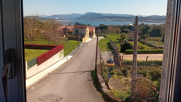A view from inside a building looking out onto a road with houses, greenery, and a body of water in the distance. - Dorm 2 between Trega and Minho A GUARDA (A Guarda)