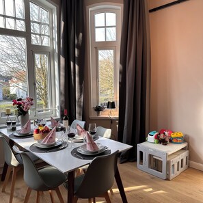 Ein Essbereich mit Tisch für vier Personen, einer Blumenvase und Blick auf Bäume durch große Fenster.