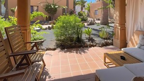 Une terrasse avec des meubles en bois, un petit jardin et un bâtiment en arrière-plan.