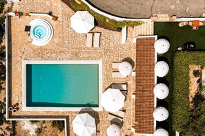 An aerial view of a swimming pool area with a stone deck, lounge chairs, umbrellas, and a wooden deck. - Mas Boronat (Salomó)