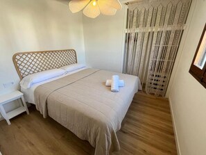 Un dormitorio con cama, mesita de noche, cortina tejida y lámpara colgante.