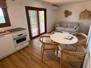 Cocina compacta con zona de comedor, sofá y un amplio ventanal corredero al exterior.