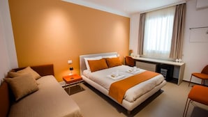 Ett hotellrum med en säng, ett skrivbord, en stol och ett fönster med gardiner.
