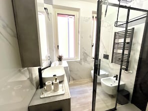 A modern bathroom with a large mirror, a sink with toiletries, a bidet, and a glass shower enclosure. - Garibaldi Living - Centro Storico Parma (Parma)