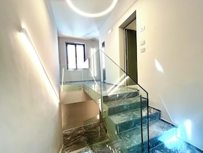 A modern staircase with glass railings and marble steps, leading to a room with a large window. - Garibaldi Living - Centro Storico Parma (Parma)