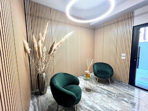 A modern interior with vertical wooden paneling, a marble floor, two green armchairs, a vase with dried plants, and a glass table. - Garibaldi Living - Centro Storico Parma (Parma)