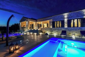 Ein modernes Haus mit Schwimmbad, Steinmauern und Außenbeleuchtung.