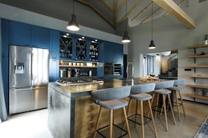 Eine moderne Küche mit blauen Schränken, einem Edelstahl-Kühlschrank, Holzbalken und Barhocker.