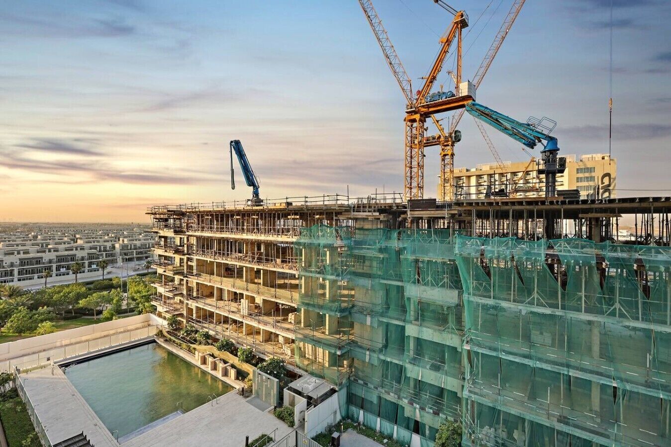 Un immeuble à plusieurs étages en construction, avec une piscine, des grues et des échafaudages.