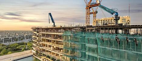 A multi-story building under construction with a pool, cranes, and scaffolding.