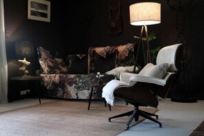 Un salón de noche con decoración oscura, un sofá, una silla, una lámpara y una mesita.