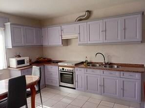 Uma cozinha com armários brancos, micro-ondas, fogão, pia e uma cadeira.