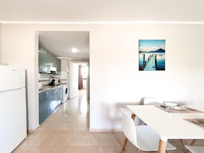 Una cucina moderna con lavatrice, zona pranzo con tavolo e sedie, e un quadro raffigurante una scena costiera.
