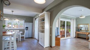 Une cuisine spacieuse avec des meubles blancs, un coin repas comprenant une table et des chaises, et une grande porte-fenêtre coulissante donnant sur une terrasse extérieure.