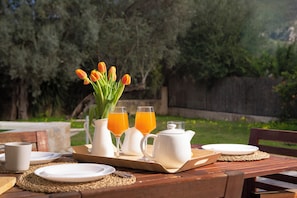 Ein Frühstücksarrangement mit Orangensaft, Tulpen und einer Kanne auf einem Holztisch im Freien.