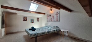 A bedroom with a sloped ceiling, a bed, a small table, and wall art. - Jacuzzi and barbecue (Saint-Hippolyte)