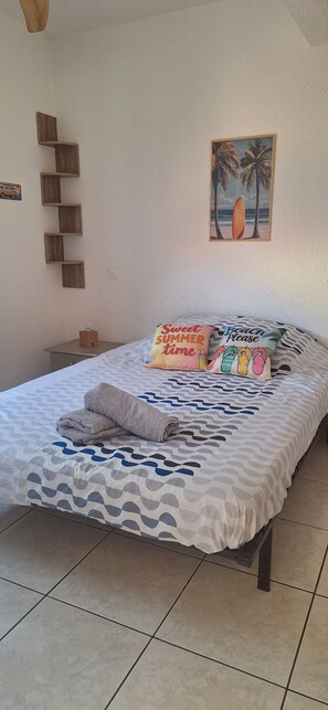 A bed with a patterned bedspread, a beach-themed pillow, and a towel. - Jacuzzi and barbecue (Saint-Hippolyte)