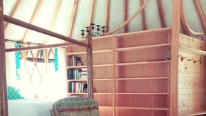 L’intérieur d’une yourte, avec un fauteuil à motifs, une bibliothèque et une table en bois.