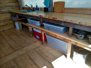 A rustic kitchen with wooden shelves, a sink, and storage containers. - Sanctuary Yurt Glamping Forest Getaway in Alberton, MT (Alberton)