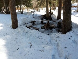 Bosque cubierto de nieve con una fogata y bancos.